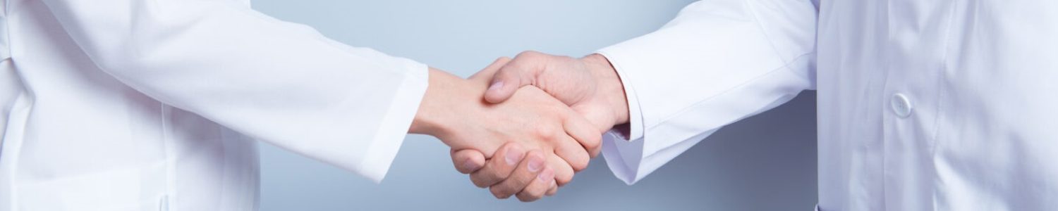 Deal! Concept of collaboration in medicine. Close up photo of two doctors' handshake on gray background